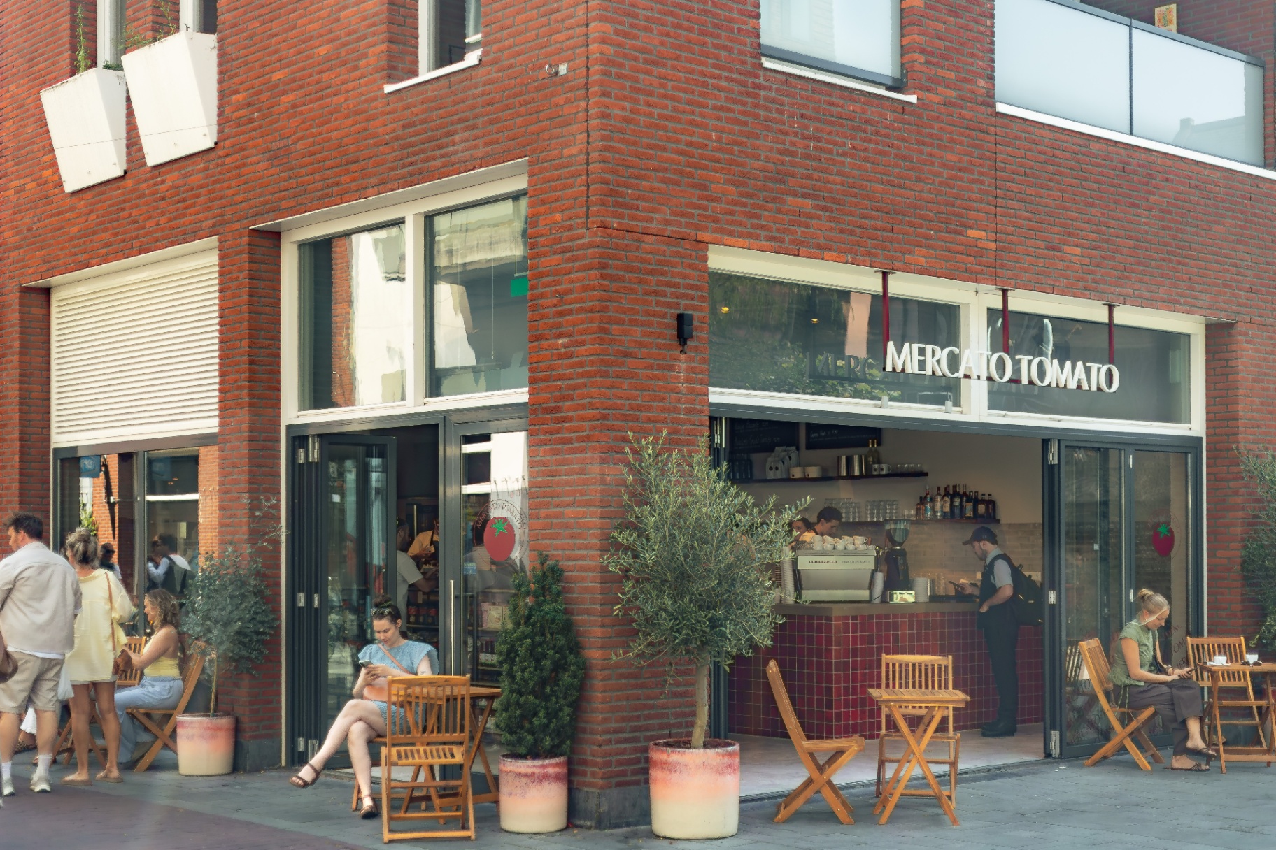 Gevel van Mercato Tomato in Haarlem met houten terrasstoelen en olijfbomen